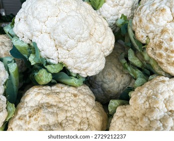 This image shows a close-up view of a pile of fresh cauliflower heads with green leaves. The cauliflowers are white and have a slightly textured surface. They appear to be freshly picked and are likely to be used in a variety of dishes, from salads to soups. The image highlights the beauty of nature's bounty and the importance of healthy eating.