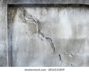 This image shows a close-up view of a weathered and aged concrete wall. The most prominent feature is a large, deep, and jagged diagonal crack running through the center of the structure.

The surface of the concrete is heavily textured, showing signs of significant wear, discoloration, and dark stains likely caused by moisture and exposure to the elements over time. The structural damage appears severe, with the concrete visibly separating and crumbling along the edges of the main fracture line, indicating potential structural instability or settling issues.