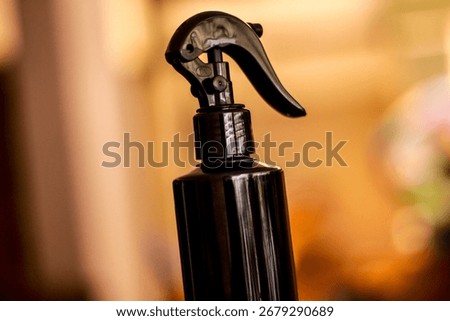 This image shows a close-up view of a dark-colored spray bottle with a sleek and modern design. The bottle features a curved trigger spray nozzle, commonly used for hair care products, cleaning soluti