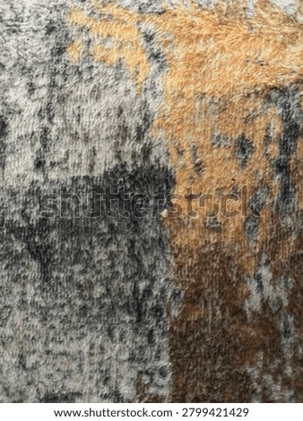 This image shows a close-up view of a rough, weathered surface with a mixture of gray, black, brown, and beige tones. The texture appears coarse and uneven, resembling natural rock, tree bark, or an aged wall. Dark patches and irregular patterns are scattered across the surface, creating a rugged and organic appearance. The lighting highlights the intricate details and fibrous textures, giving the image a highly textured and abstract look