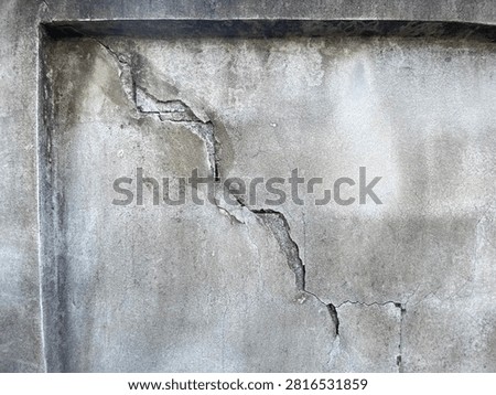 This image shows a close-up view of a weathered and aged concrete wall. The most prominent feature is a large, deep, and jagged diagonal crack running through the center of the structure.

The surface of the concrete is heavily textured, showing signs of significant wear, discoloration, and dark stains likely caused by moisture and exposure to the elements over time. The structural damage appears severe, with the concrete visibly separating and crumbling along the edges of the main fracture line, indicating potential structural instability or settling issues.