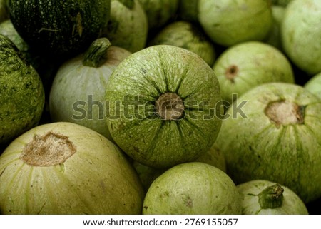 This image shows a cluster of round, pale green summer squashes, commonly known as round zucchini, eight ball squash, or calabacita. They feature smooth, slightly speckled skin and are shown from a top-down perspective, emphasizing their organic texture and shape.
