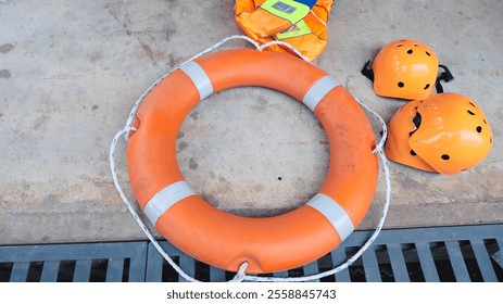 This image shows essential safety equipment including an orange life ring, life jacket, and helmets on a concrete surface, highlighting the importance of safety in water-related activities. - Powered by Shutterstock