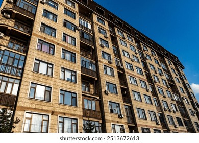 This image shows the exterior of a modern high-rise apartment building with a combination of brick and glass facade. Set against a bright blue sky, the building features large windows and multiple bal - Powered by Shutterstock