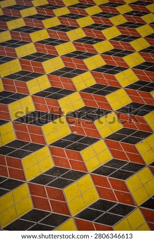 This image shows a floor covered in square tiles arranged in a repeating pattern that creates an optical illusion of three-dimensional cubes. The 