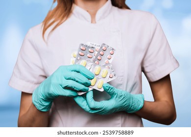 This image shows a healthcare professional wearing a white coat and green gloves, holding several blister packs of medication. The focus on the hands and medication packs emphasizes the handling. - Powered by Shutterstock