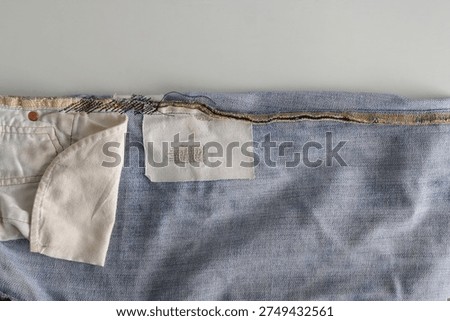 This image shows inside out of a pair of jeans, showcasing a functional under-layer patch designed to reinforce a worn area and extend the garment's lifespan. By securing a piece of white fabric behind the denim with a dense stitch, this repair acts as a powerful statement of sustainability and conscious consumption, directly diverting textile waste from landfills. This method prioritizes the circular economy by valuing durability over disposability, showing how a simple structural mend can significantly reduce the environmental footprint associated with producing new denim.