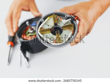 This image shows the internal components of an electric motor or starter motor held in a hand, revealing the field windings, carbon brushes, and wires. A screwdriver is visible in the background.