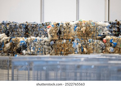 This image shows large bundles of compressed recycled plastic materials, stacked in a warehouse or recycling facility.  - Powered by Shutterstock