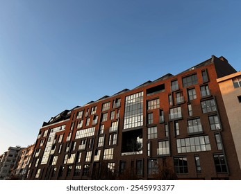 This image shows a modern brick apartment building with large glass windows, set against a clear blue sky. - Powered by Shutterstock