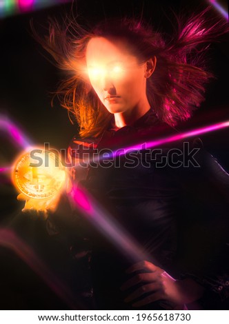 This image shows a powerful young woman holding a glowing crypto currency Bitcoin in her palm as her eyes beam lasers into a dark room. 