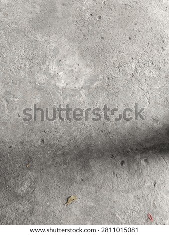 This image shows a rough, weathered grey concrete surface, likely an outdoor ground or pavement. Its texture is uneven and gritty, with faded patches, faint scratches, and small pits from long-term use.