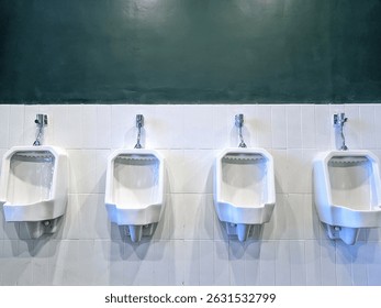 This image shows a row of four white ceramic urinals mounted on a tiled wall in a public restroom. The upper part of the wall is painted dark green, while the lower part features white vertical tiles.