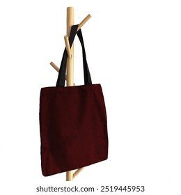 This image shows a simple tote bag in dark red fabric with black straps, hanging on a wooden coat rack. The tote bag has a rectangular shape, no visible designs or patterns,and a minimalist appearance - Powered by Shutterstock