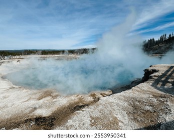 This image shows a steaming hot spring in Yellowstone, with vibrant blue water surrounded by mineral deposits under a clear sky. A serene wilderness scene with trees in the distance. - Powered by Shutterstock