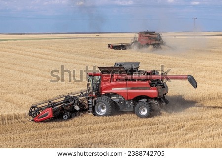 This image shows a two red combines, part of the team of men and machines harvesting the ripened grain on a large farm in the western Canadian prairie area.   