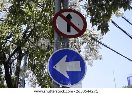 This image shows two traffic signs mounted on a pole. The top sign, with a red border and a black arrow crossed out, indicates 