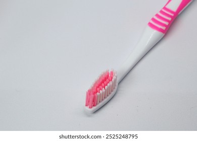 This image shows a white toothbrush with a pink accented handle and partially pink bristles. The design is simple, with an ergonomic handle and soft bristles. - Powered by Shutterstock