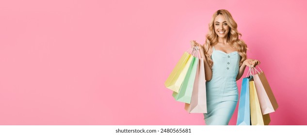 This image shows a young woman standing in front of a pink background, holding a collection of colorful shopping bags. She is smiling brightly and appears to be happy with her purchases. - Powered by Shutterstock