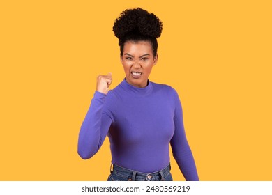 This image shows a young woman with dark skin and a determined expression. Her hair is styled in a high bun, and she is wearing a purple long-sleeved shirt and jeans. - Powered by Shutterstock