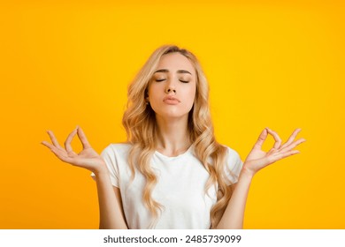 This image shows a young woman with long blonde hair, wearing a white T-shirt, practicing meditation with her eyes closed. She has her hands raised in a peaceful gesture - Powered by Shutterstock