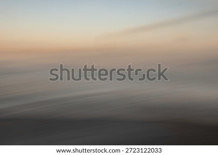 This image is a sophisticated example of Intentional Camera Movement (ICM) photography, capturing a serene and ethereal seascape at the transition of twilight. The composition is defined by its soft, painterly quality, where the traditional boundaries between sea, sky, and shore are dissolved into a fluid arrangement of horizontal bands. The color palette is exceptionally delicate, featuring a gradient of muted oceanic blues, hazy grays, and a warm, glowing amber horizon that suggests the final moments of a sunset or the first light of dawn.

The long exposure and deliberate panning motion create a rhythmic sense of movement, transforming the crashing waves into a series of soft, atmospheric streaks. This abstraction emphasizes the emotional resonance of the coast—tranquility, solitude, and the ephemeral nature of time—rather than its literal details. The subtle textures within the blur give the piece a tactile, canvas-like feel, making it an ideal choice for high-end interior decor, meditative editorial content, or minimalist graphic design backgrounds.

There is a profound sense of stillness despite the implied motion. The heavy, dark tones at the bottom provide a grounded foundation, while the lighter, airy hues at the top evoke a sense of vastness and possibility. This balance of light and shadow, combined with the dreamlike aesthetic, allows the viewer to project their own narrative onto the scene. It is a visual representation of 