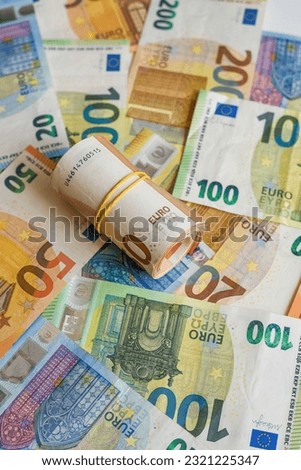 This image is of a stack of euro bank notes, with one of them rolled up and another partially rolled up
