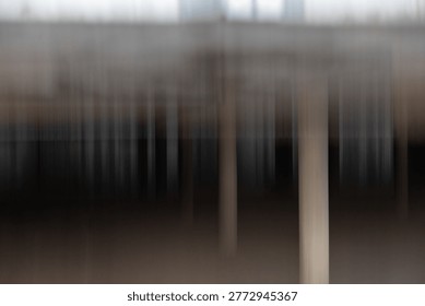 This image is a striking example of Intentional Camera Movement (ICM), featuring a vertical motion blur that transforms a physical structure - likely a pier, bridge, or industrial colonnade - into a rhythmic, abstract composition. The palette is grounded in muted earth tones, deep charcoals, and hazy greys, creating a sense of layered depth. The interplay of light and shadow produces a 