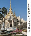 This image a stunning view of a Thai temple with intricate golden spires, surrounded by lush greenery and vibrant flowers. The peaceful atmosphere is enhanced by a fountain at the temple