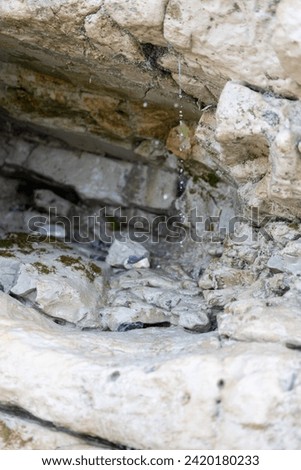 This image zooms in on a small, intimate scene where water gently drips from an overhang of limestone rock. The camera captures the droplets in mid-fall, creating a visual melody that resonates with
