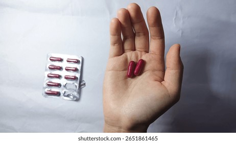 This impactful close-up features two vibrant red medicine capsules held gently in a hand, creating a powerful visual representation of health, treatment, and personal care.