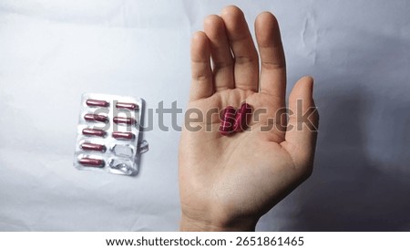 This impactful close-up features two vibrant red medicine capsules held gently in a hand, creating a powerful visual representation of health, treatment, and personal care.