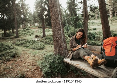 This is important. Portrait of beautiful young lady writing in notebook and smiling. Trees and green plants on background - Shutterstock ID 1191541345