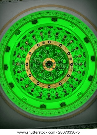 This is the interior of a mosque dome, featuring Islamic art and green hues adorning the ceiling of the dome.