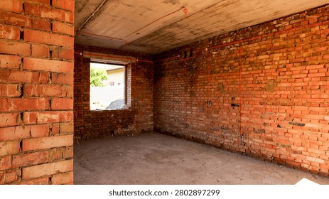This is an interior view of a construction site, showcasing red brick walls, a concrete ceiling with visible electrical conduits, and an empty room awaiting finishing touches