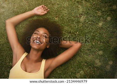 This is the life. Shot of a young woman laughing while relaxing on the grass.
