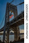 This low angle shot highlights the iconic George Washington Bridge, with a large American flag fluttering in the foreground