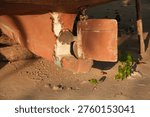 This low-angle shot captures the underside of a boat, featuring its propeller and rudder. The red hull shows some wear and tear, with a small green plant growing nearby.