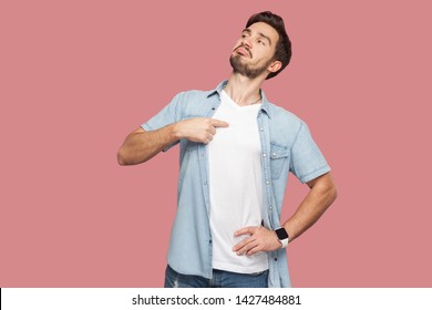 This is me. Portrait of proud haughty handsome bearded young man in blue casual style shirt standing, looking away and pointing himself. indoor studio shot, isolated on pink background. - Shutterstock ID 1427484881