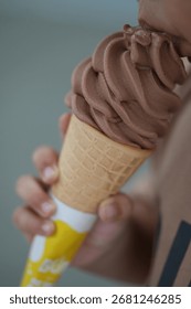This mid-air bite of chocolate soft serve captures pure snack-time joy. With its swirl, yellow-white wrapper, and blurred background, it feels like a sweet, stolen second in the sun.