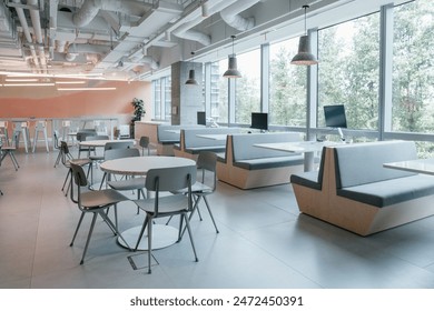 This modern office space features an open, airy design with large windows providing ample natural light and a view of lush greenery outside. - Powered by Shutterstock