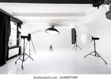 This modern studio features a white cyclorama wall and professional lighting equipment arranged for a photoshoot. A single stool is positioned as a focal point for models or subjects.