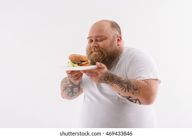 This is my favorite food. Joyful fat man is smelling sandwich and smiling. His eyes are closed with pleasure. Isolated and copy space in left side