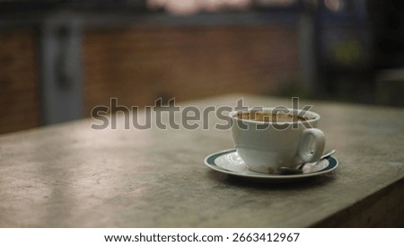 This nighttime landscape image captures a single cup of coffee placed on a cement table, set against a softly blurred bokeh background. The composition thoughtfully employs the rule of thirds