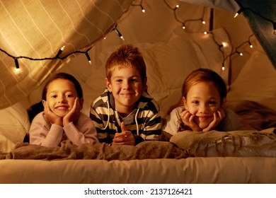 This is our blanket fort. Shot of three young children in a tent together.