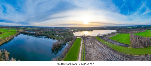 This panoramic aerial photograph captures a breathtaking view of a lakeside scene at sunset. The sprawling landscape includes a large, reflective lake bordered by lush trees and a patchwork of - Powered by Shutterstock