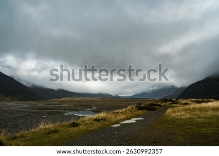 
This panoramic shot captures a vast, rugged valley under a dramatic, cloudy sky, with mountains shrouded in mist and a river snaking through the desolate landscape. It evokes a sense of raw nature.