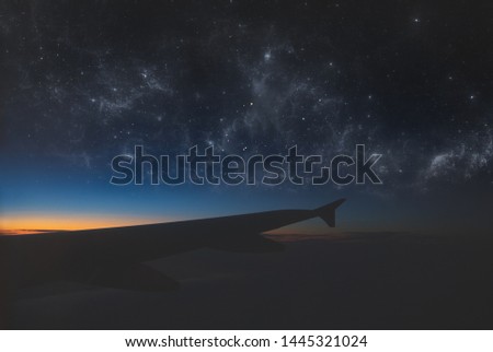 This is a photo of from the air of a nigth sky, with stars and constellations. The sunrise is coming and the wing of a airplane is in frame too.