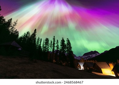 This photo captures the breathtaking northern lights (Aurora Borealis) illuminating the night sky above a mountain village with vibrant colors over snow-capped peaks and wooden cabins. - Powered by Shutterstock