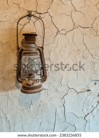 This photo captures the warm glow of an oil lamp against a mud wall. The lamp is suspended from a wooden beam, and its flame casts a soft light on the wall. 